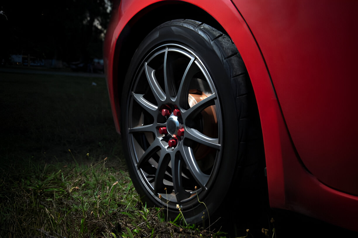 Red car wheel with sleek alloy rim and red lug nuts on grassy ground