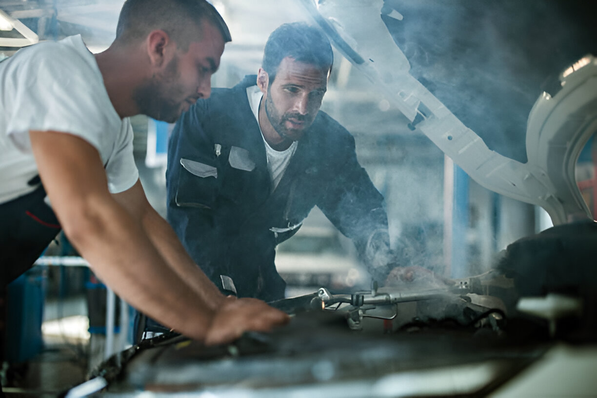 Two mechanics working on a vehicle engine in a smoky repair shop