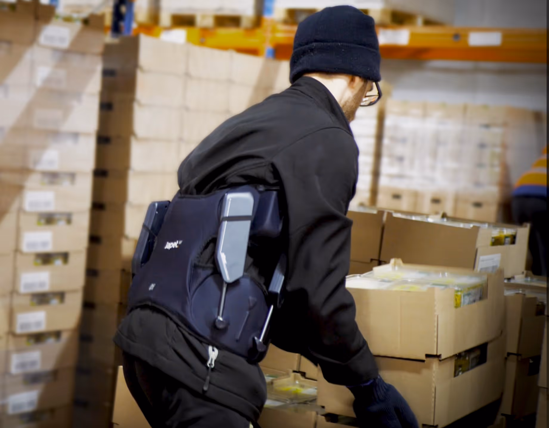 Un préparateur de commande dans un entrepôt logistique porte un exosquelette pour protéger son dos