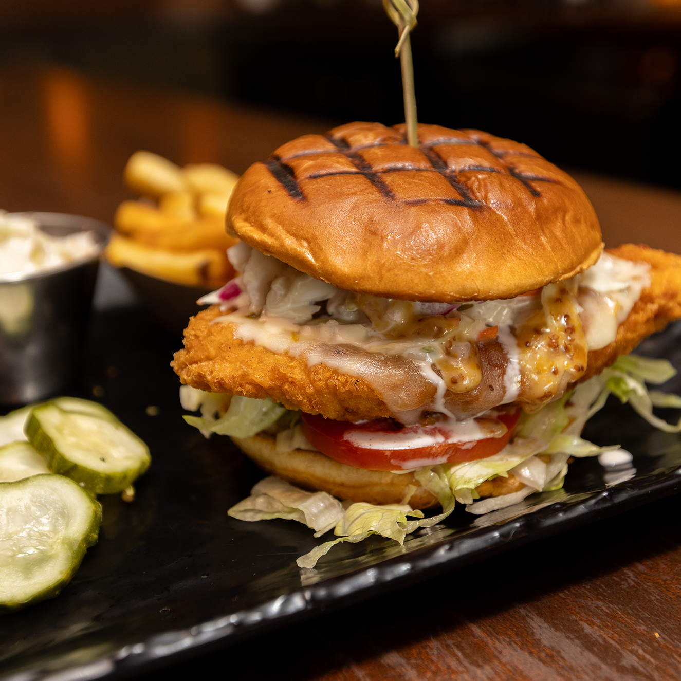 Close up of a fried chicken sandwich served with pickles, coleslaw, and french fries on a black plate