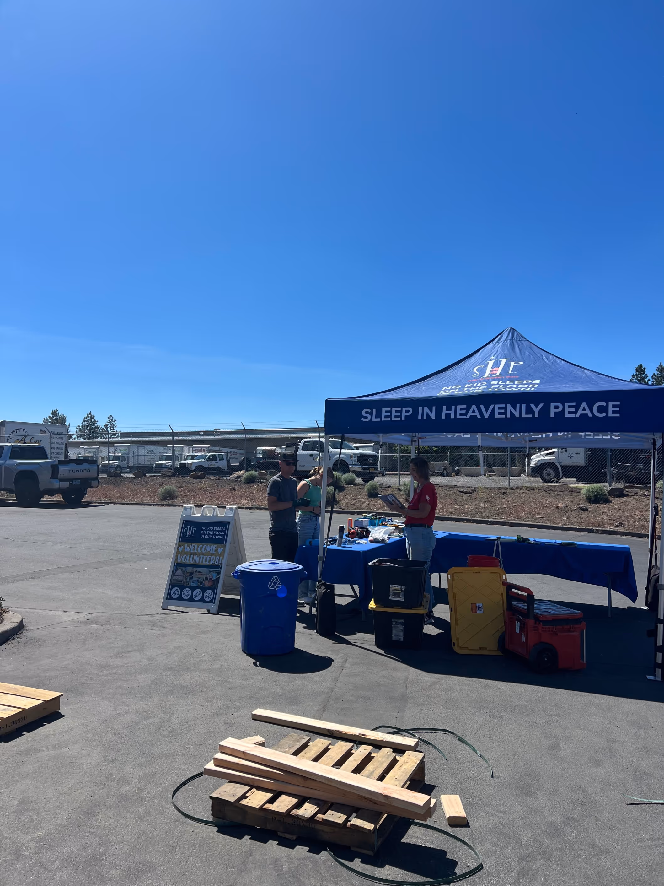 Volunteers at the Sleep in Heavenly Peace event prepare materials under a blue tent on a sunny day.

