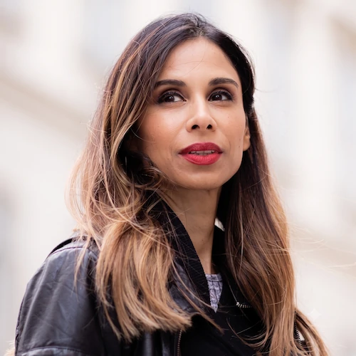 Portrait of a woman with long hair wearing a black jacket looking slightly upward outdoors.