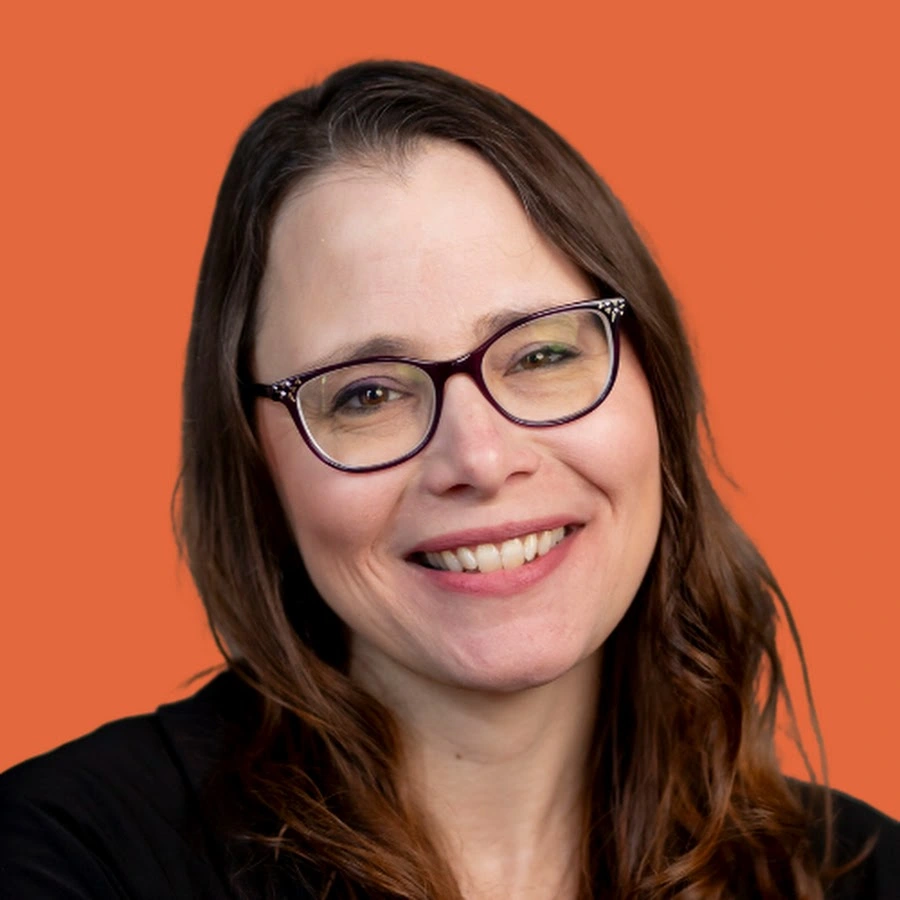Smiling woman with brown hair and glasses against an orange background.