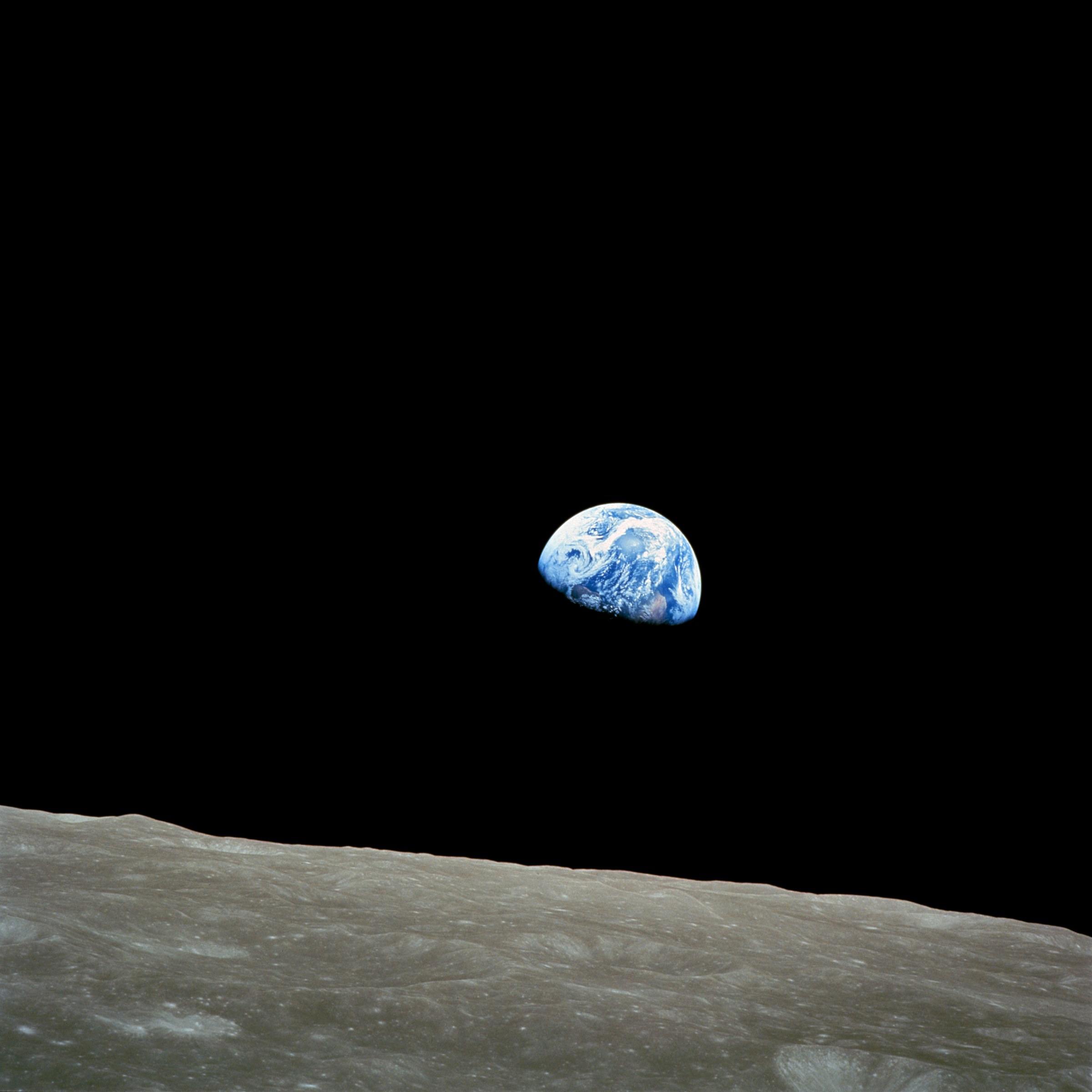 Earth rising above a cratered lunar horizon, photographed from Apollo 8.