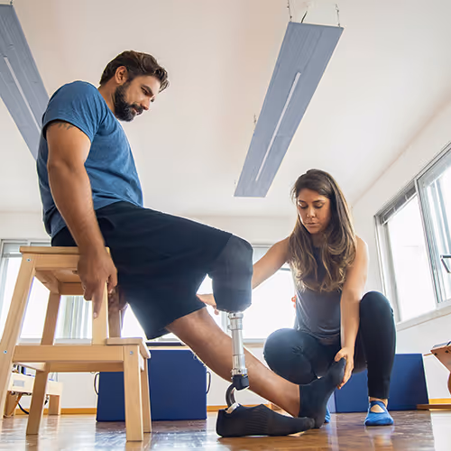 A physiotherapist assists an amputee with leg exercises.