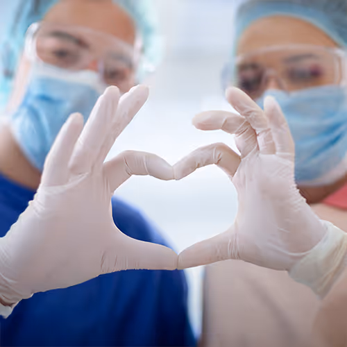 Two surgery doctors create a heart shape with their hands.