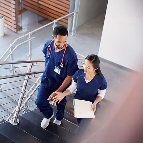 Two healthcare providers walk up stairs while talking.