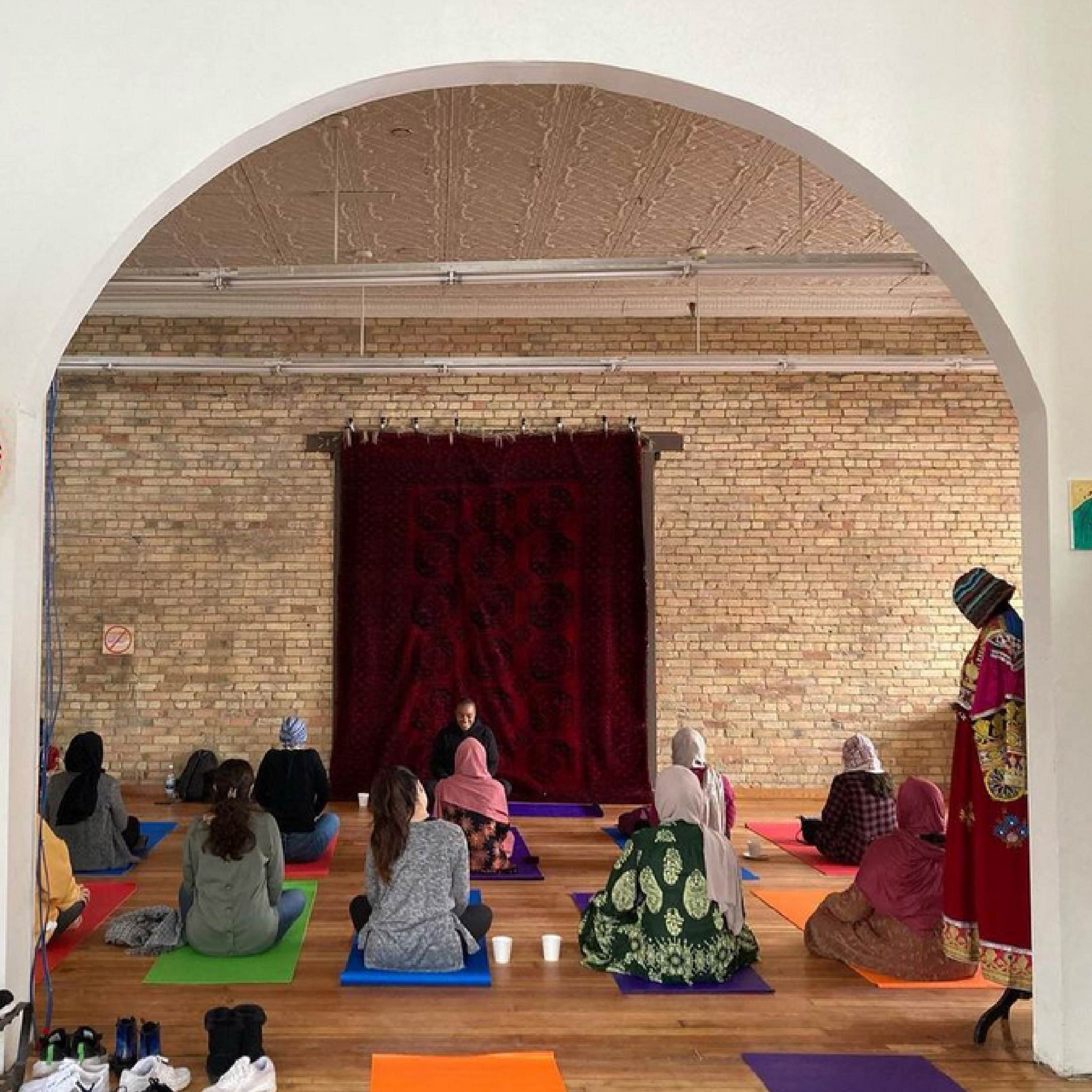 A group of women are seated for a yoga class.