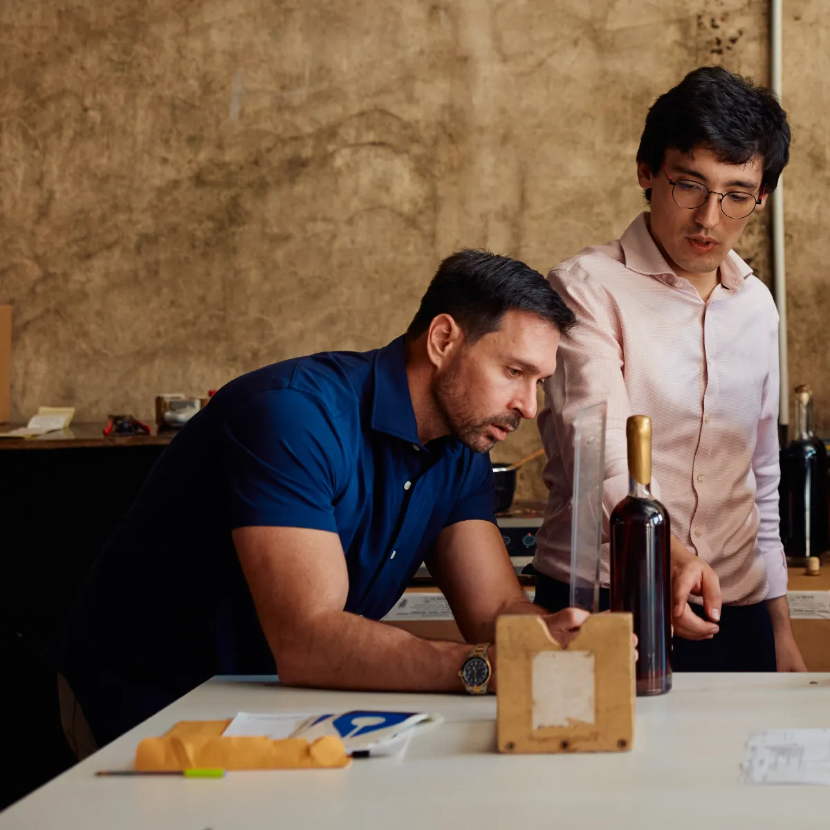 Two men evaluating an Armagnac cask sample beside a bottle.