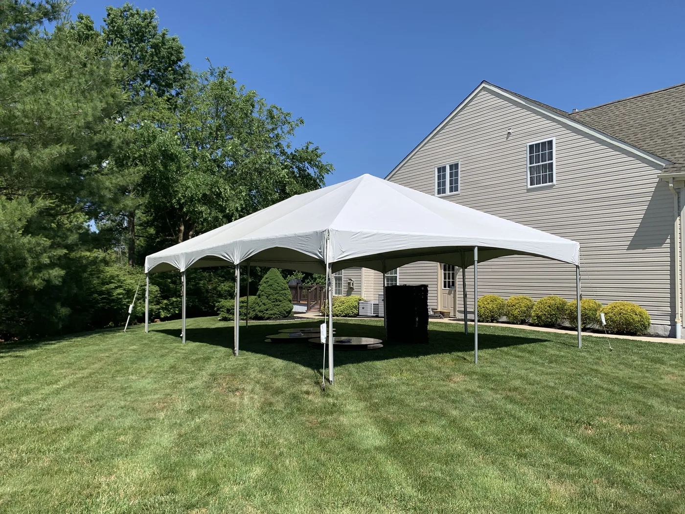 HPR backyard frame tent installed on a lawn with stacked tables ready for setup.