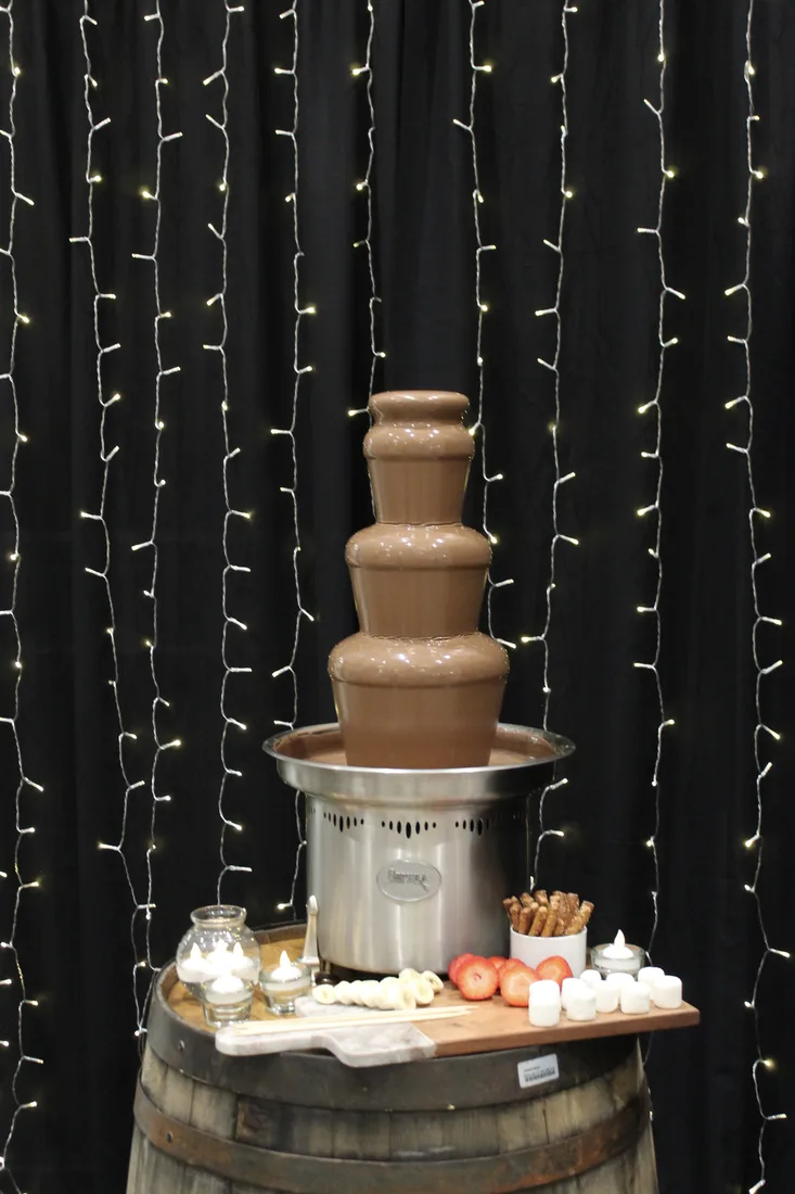 HPR chocolate fountain display set in front of a curtain of warm string lights.