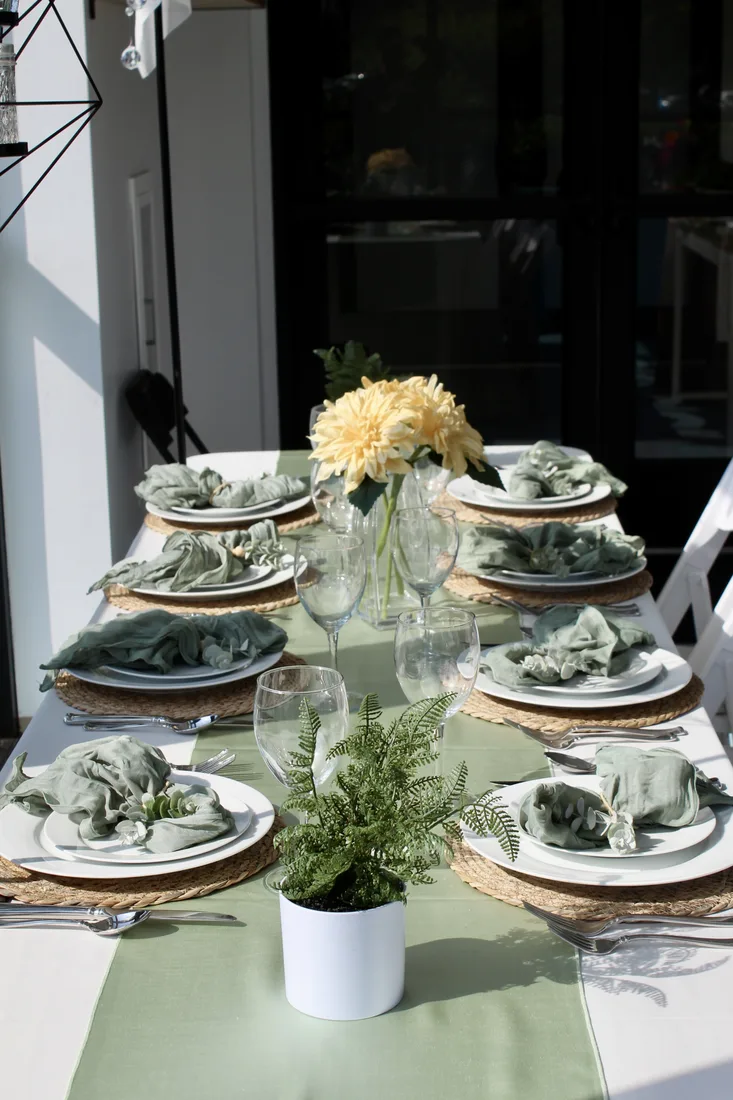 HPR table set for eight with sage linens, white plates, glassware, and low floral arrangements.