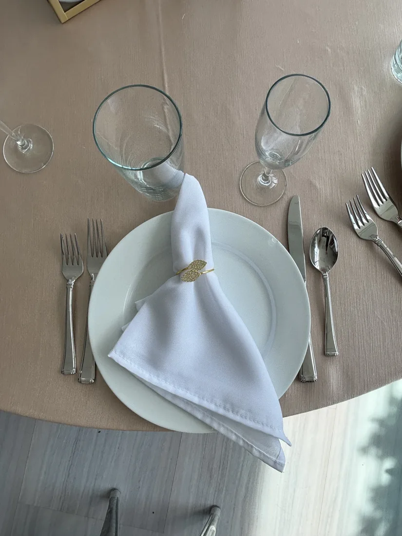 HPR place setting with a white plate, folded white napkin, glassware, and flatware on a round table.