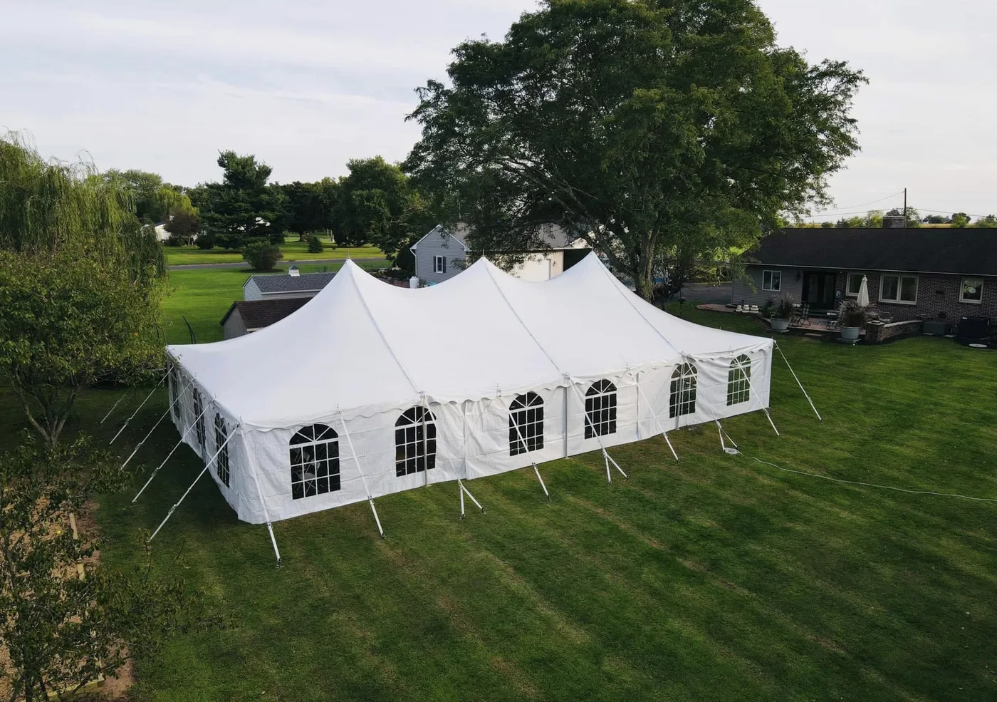 Aerial HPR project photo of a large white tent with windowed sidewalls on a backyard lawn.