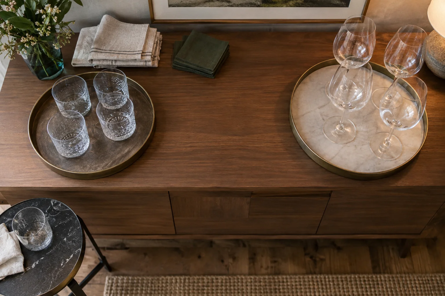 Clean tumblers and stemmed glasses grouped on separate trays, with an open workspace and a used glass on a side table.