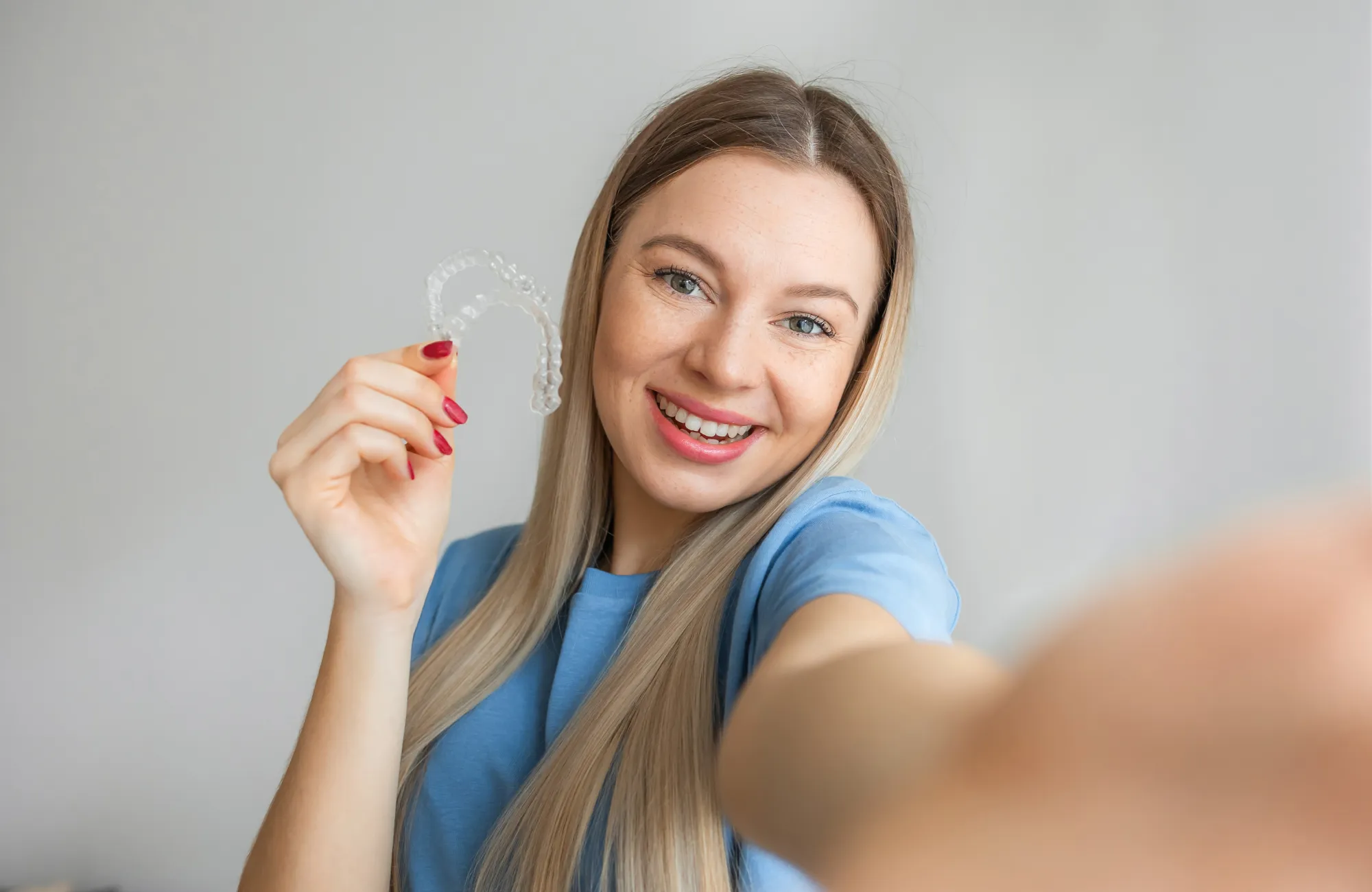 A woman sits in a dental chair, holding her cheek while a dentist prepares for examination.