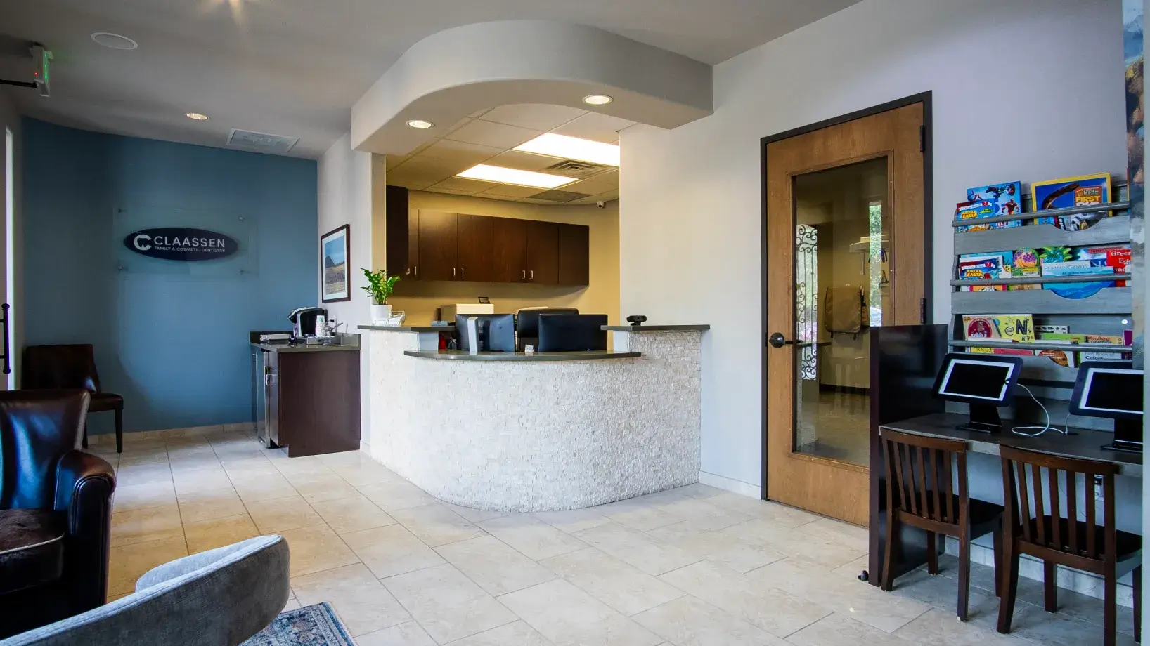 A dentist talks to a patient sitting in a dental chair with a screen showing x-rays.