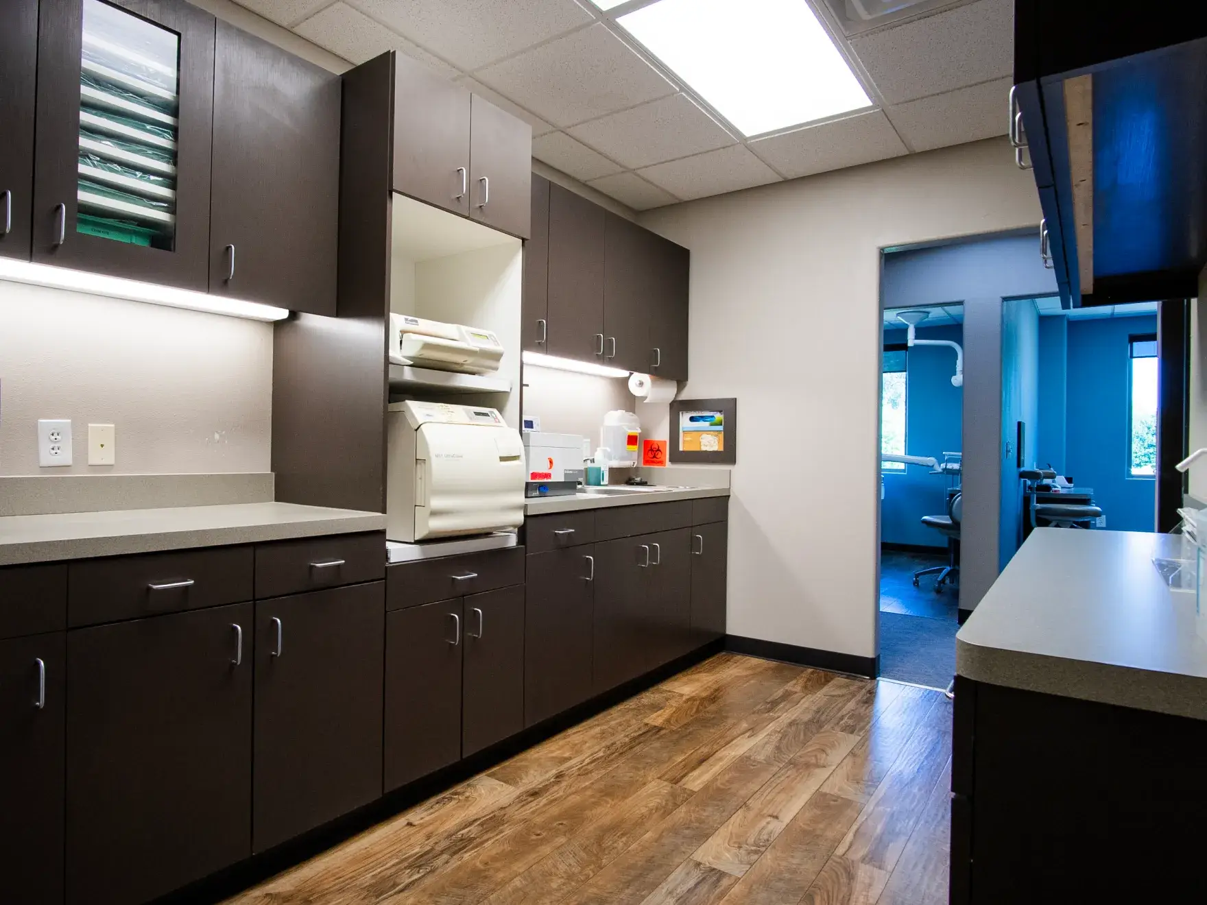 A modern dental office lab with cabinets, countertop, sterilizers, and a doorway to an exam room.