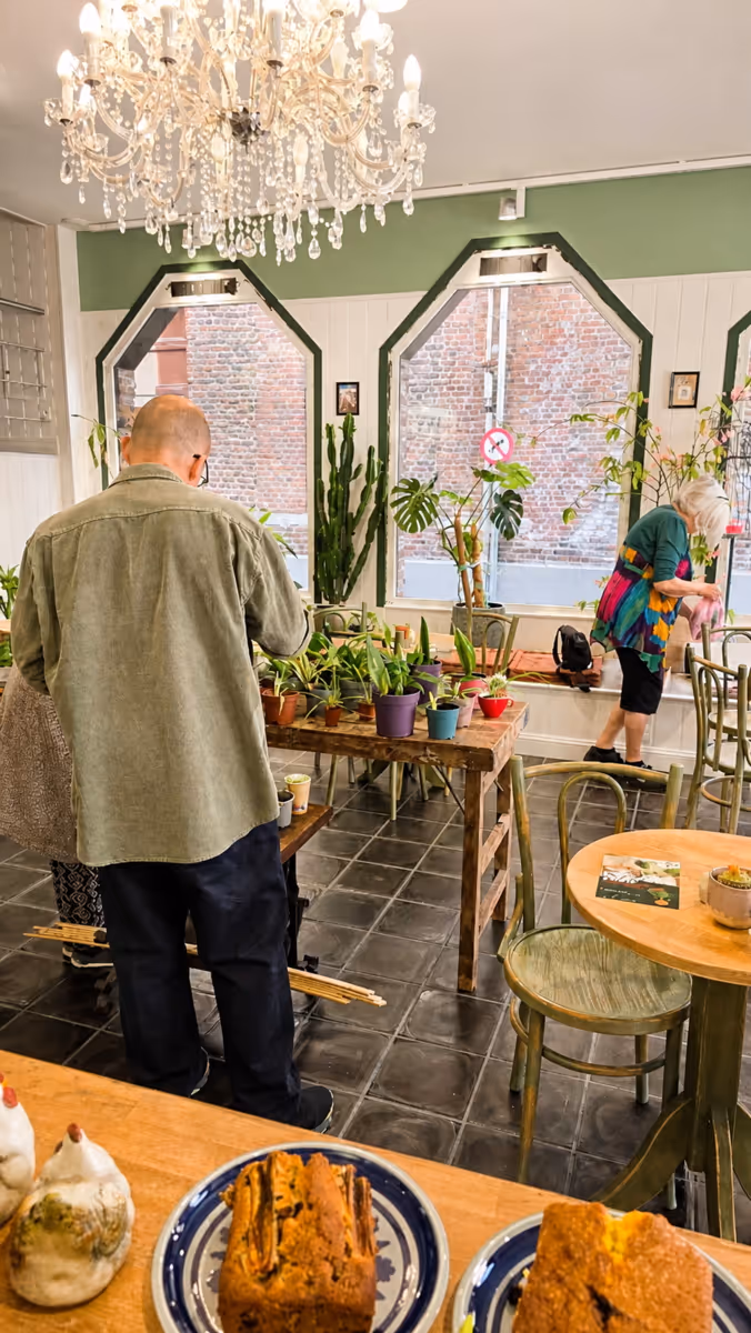 Mensen bekijken en verzorgen planten op tafels in een lichte kamer met grote ramen en een kroonluchter.