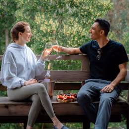 A couple toasting two wine glasses together in nature.