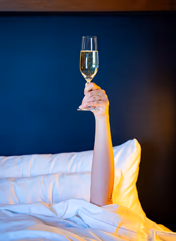 Someone's arm sticking out from under a hotel comforter with a glass of champagne.