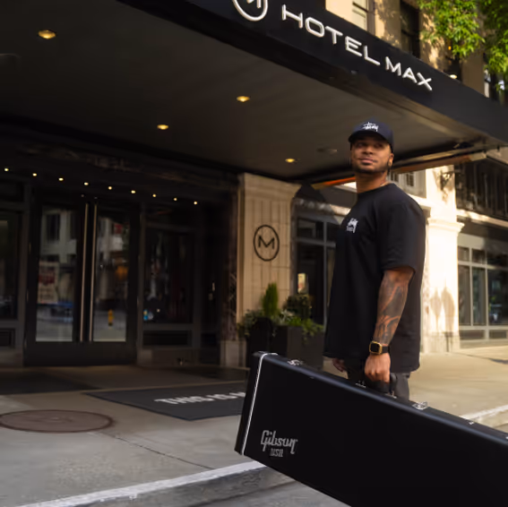 A man holding a case for an instrument in front of a venue.