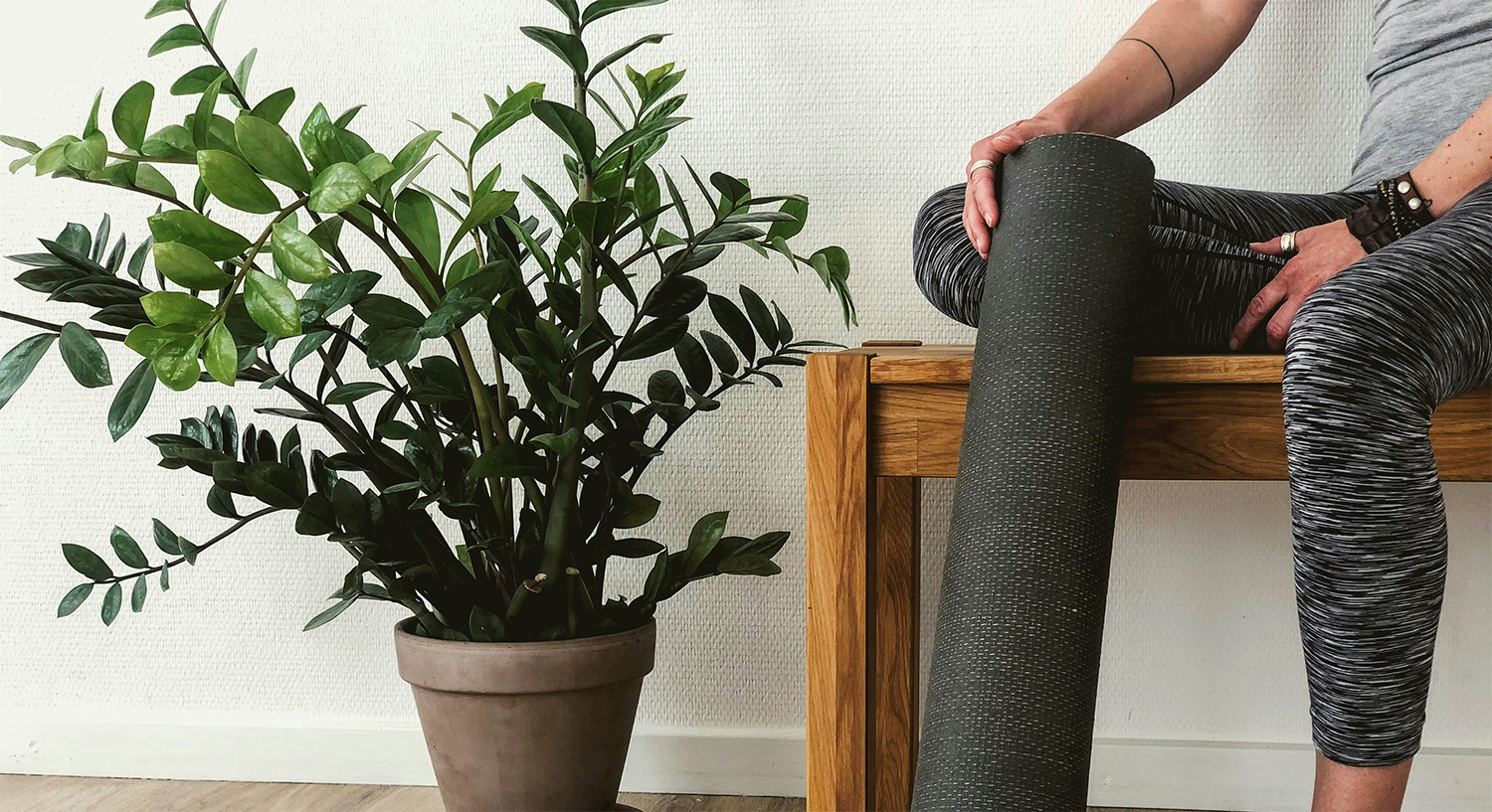 Bozeman wellness professional preparing for a yoga class, holding a mat beside a plant, symbolizing balance between health services and business growth.