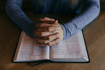 Hands folded in prayer over an open Bible on a wooden table, symbolizing faith and stewardship in church life.