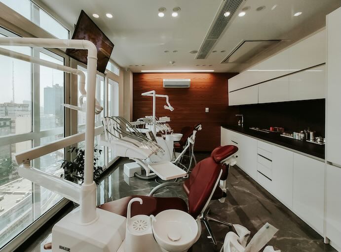 Bright, modern dental clinic with red treatment chairs, large windows, and clean white cabinetry.