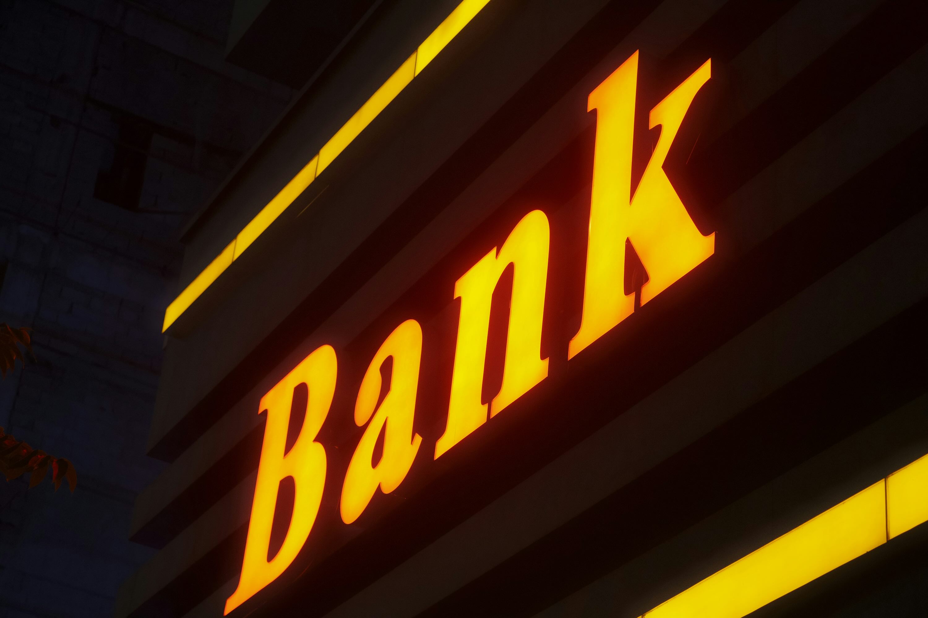 ChatGPT said: Neon yellow “Bank” sign glowing on a building at night.