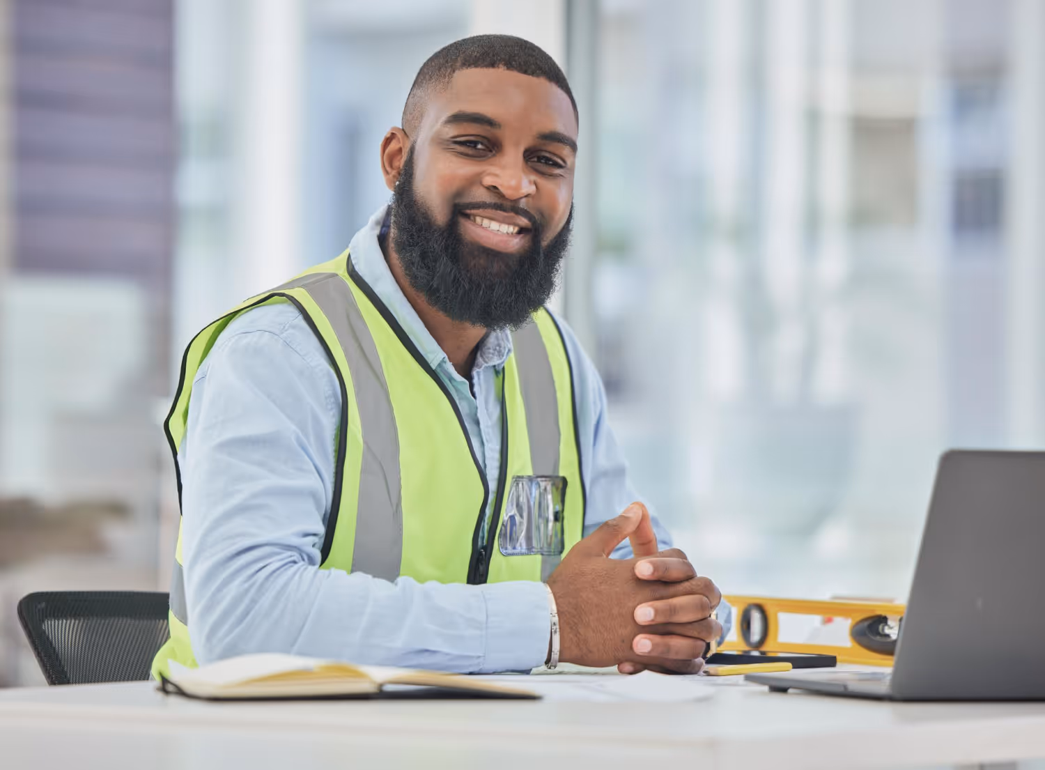 Surveyor smiling at desk with laptop and level
