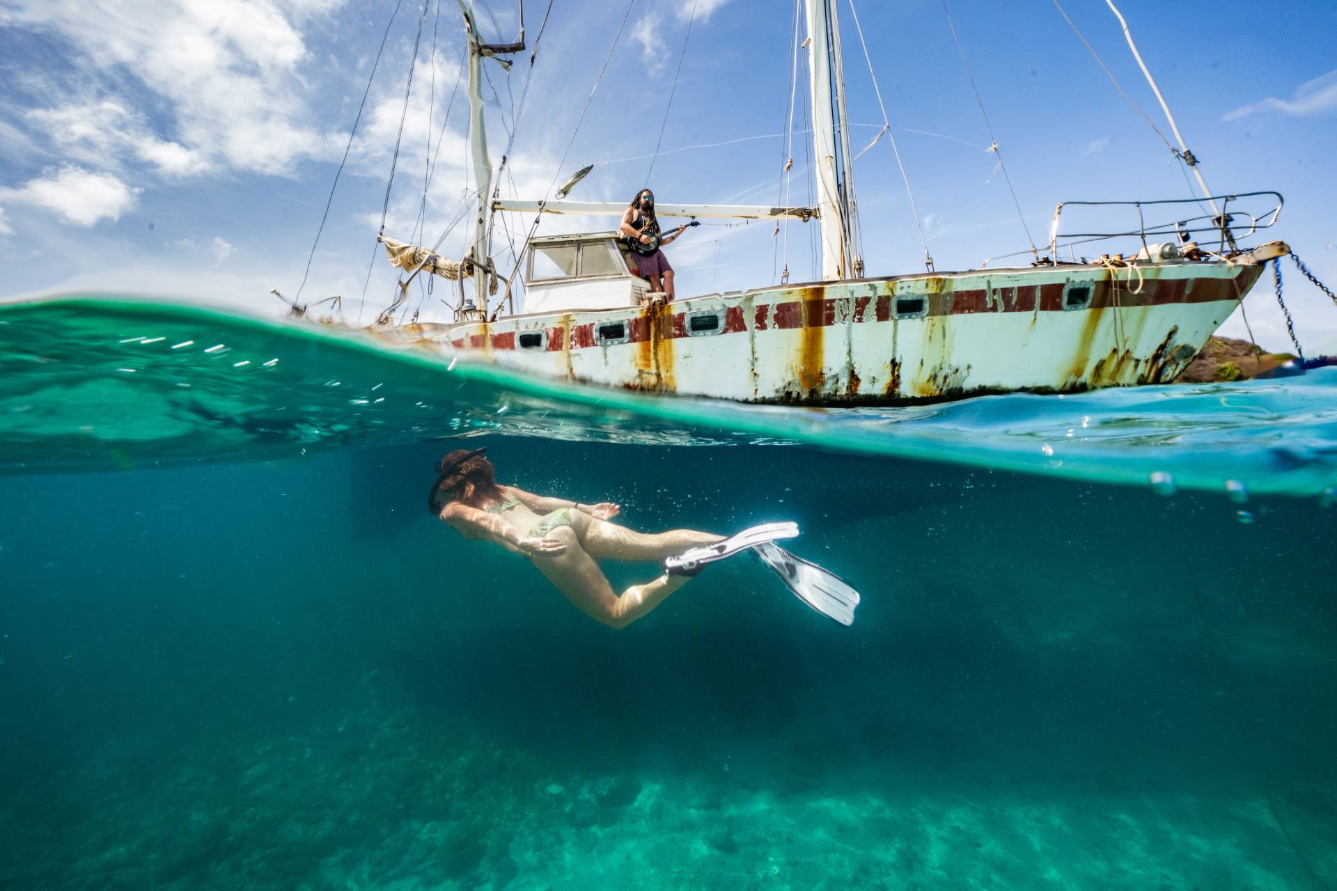 Torrin Daniels playing the banjo on a boat while a girl snorkels below him