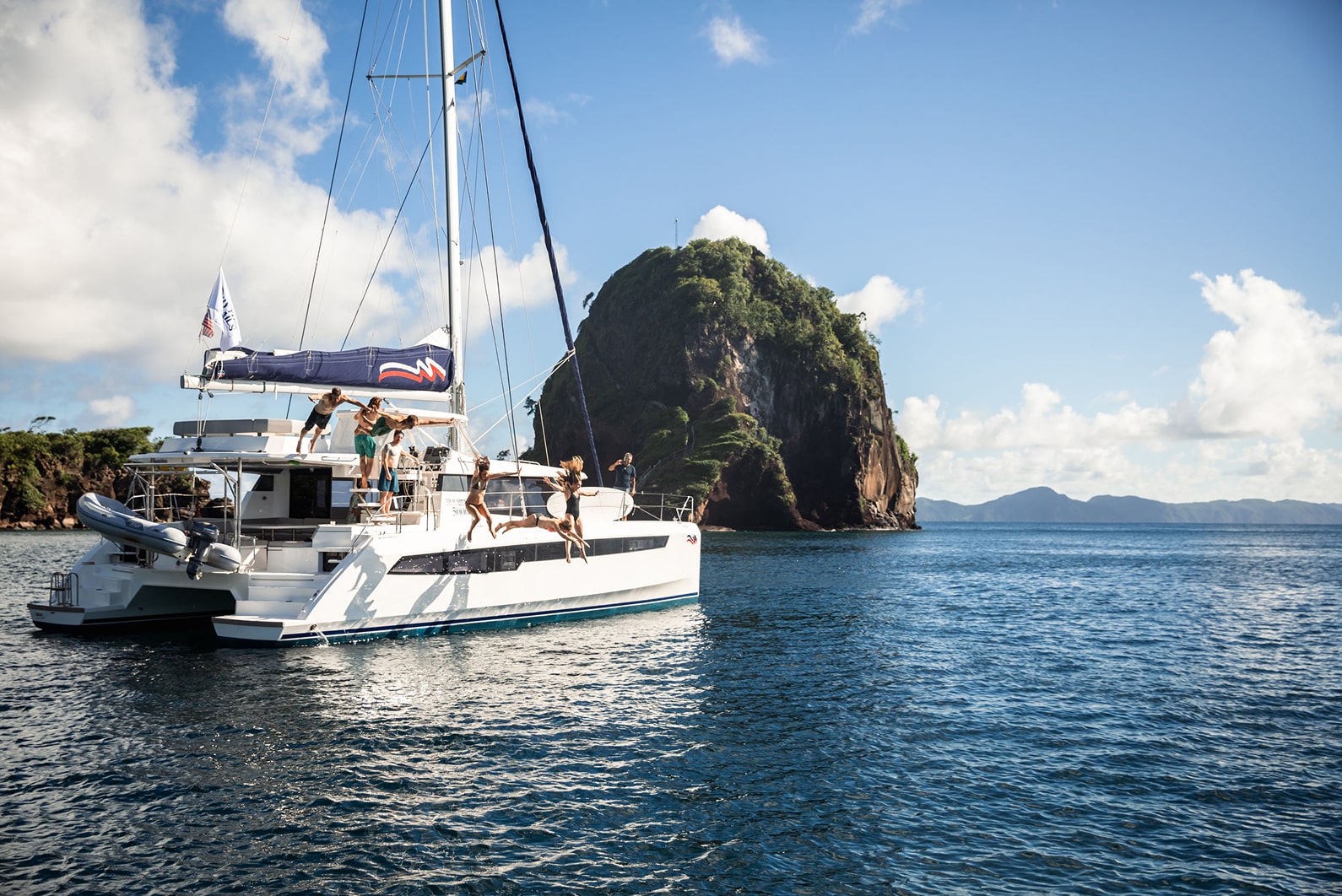 Group of friends jumping off the side of a catamaran