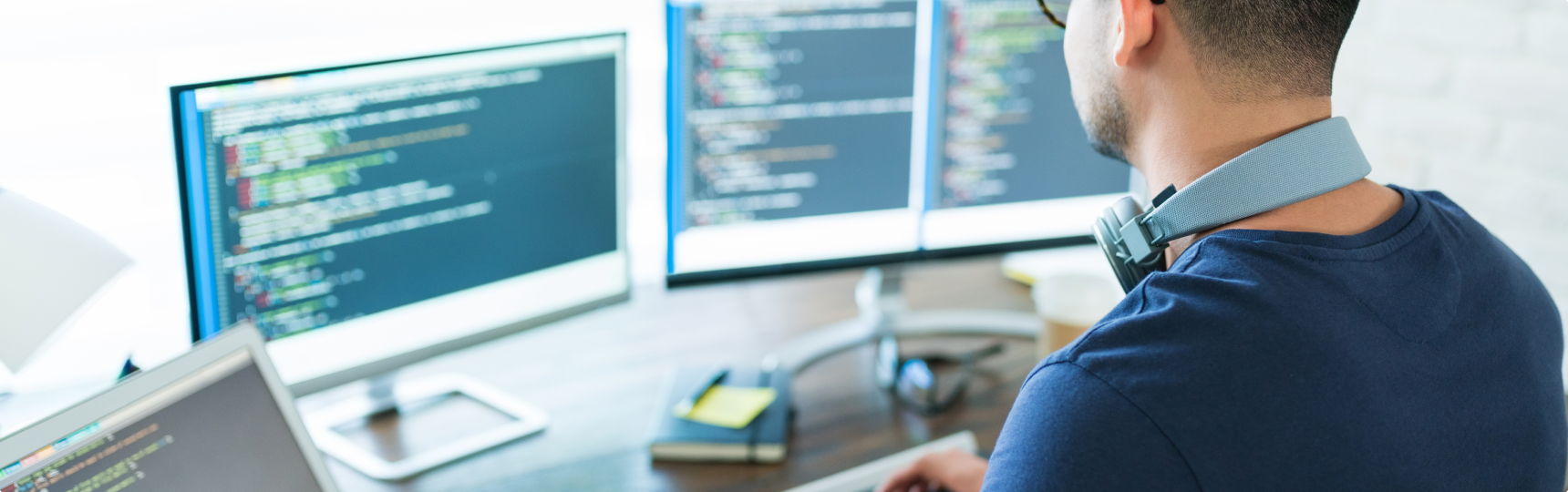Man sitting at a desk, with two computer screens showing lines of code.