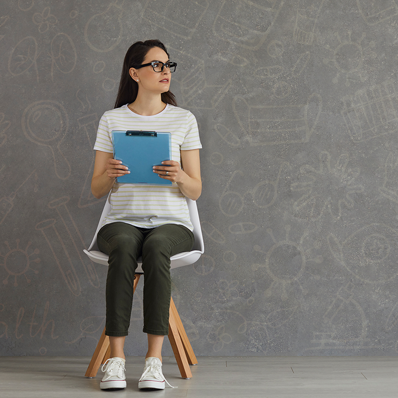 Woman sitting alone in a waiting room holding a clipboard.