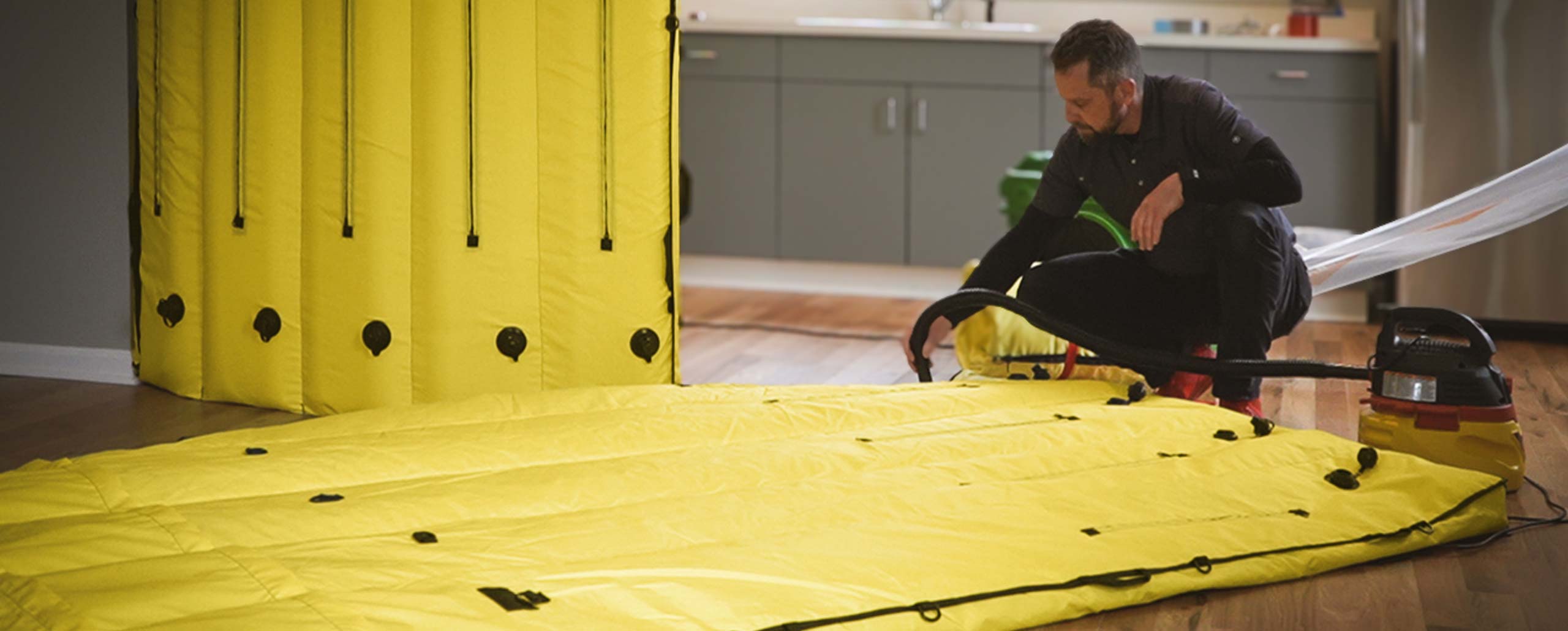 Man setting up a large yellow inflation barrier inside a room with wooden flooring.