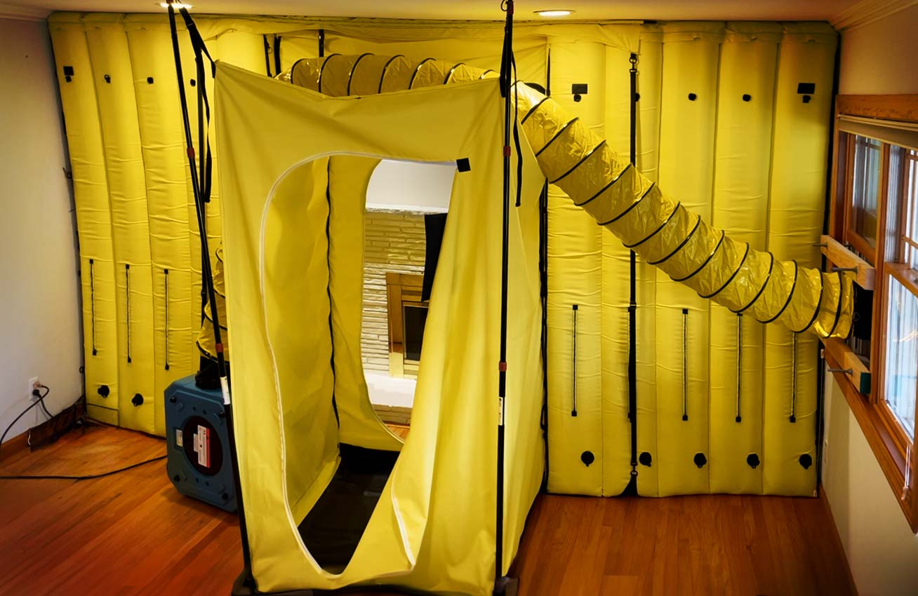 Yellow inflatable air containment system installed inside a room with wooden flooring and a window.