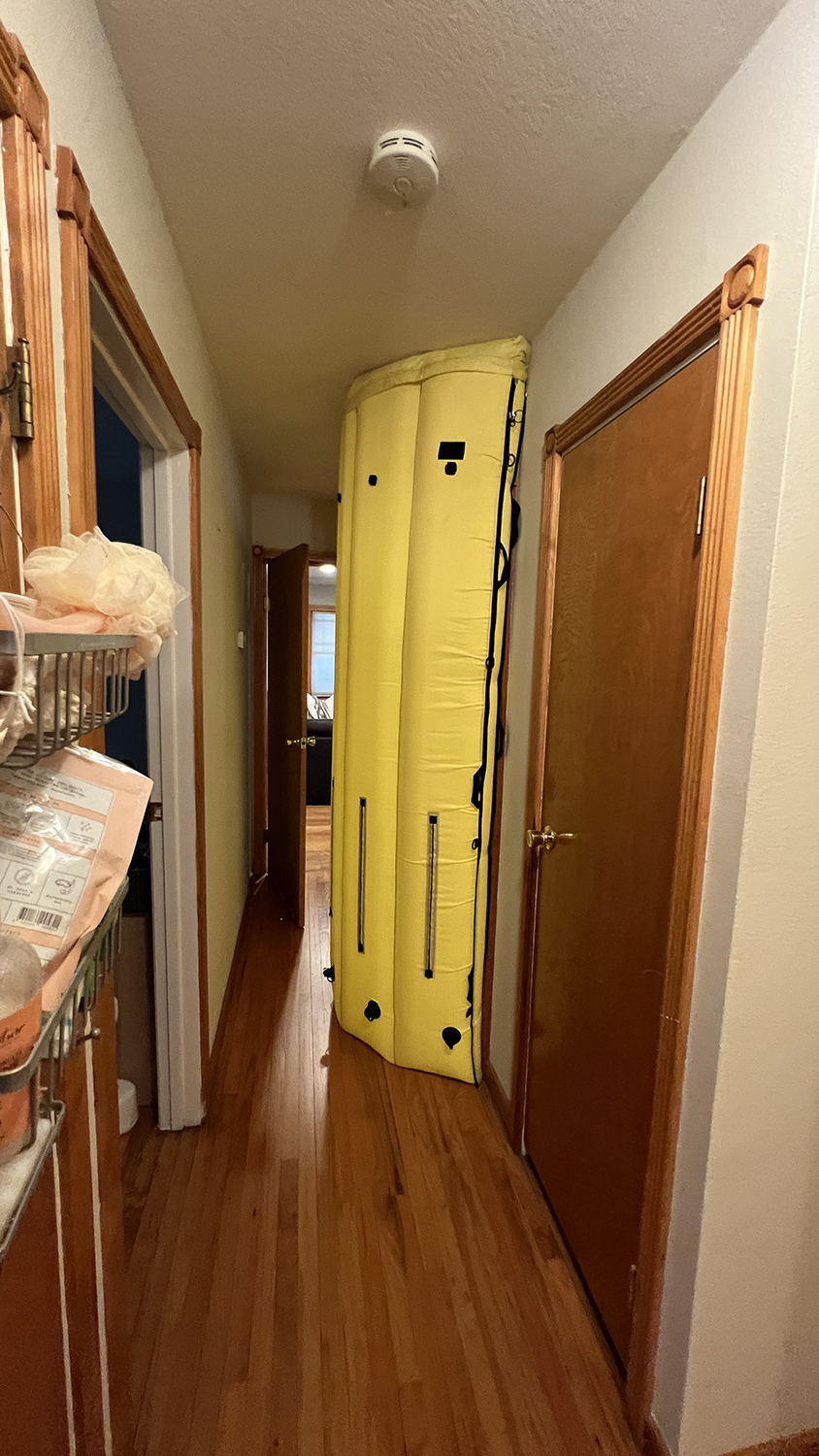 Tall yellow inflatable door frame standing upright in a narrow hallway with wooden floors and doors.