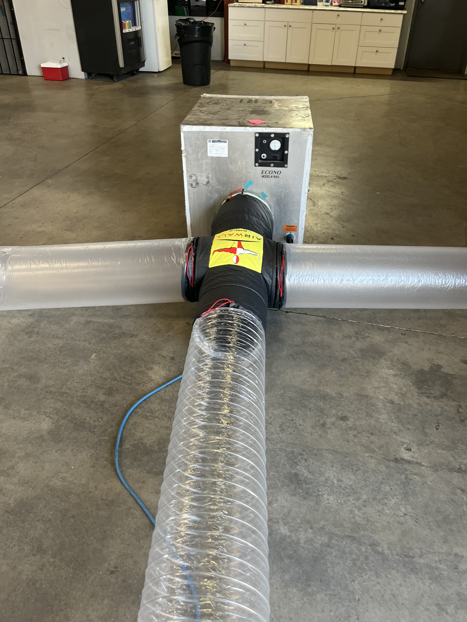 Air filtration system with clear plastic ducting and a metal unit labeled ECONO in a garage-like room.