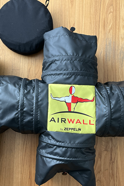 Black AirWall inflatable training dummy by Zeppelin placed on wooden floor with a black round carrying bag nearby.