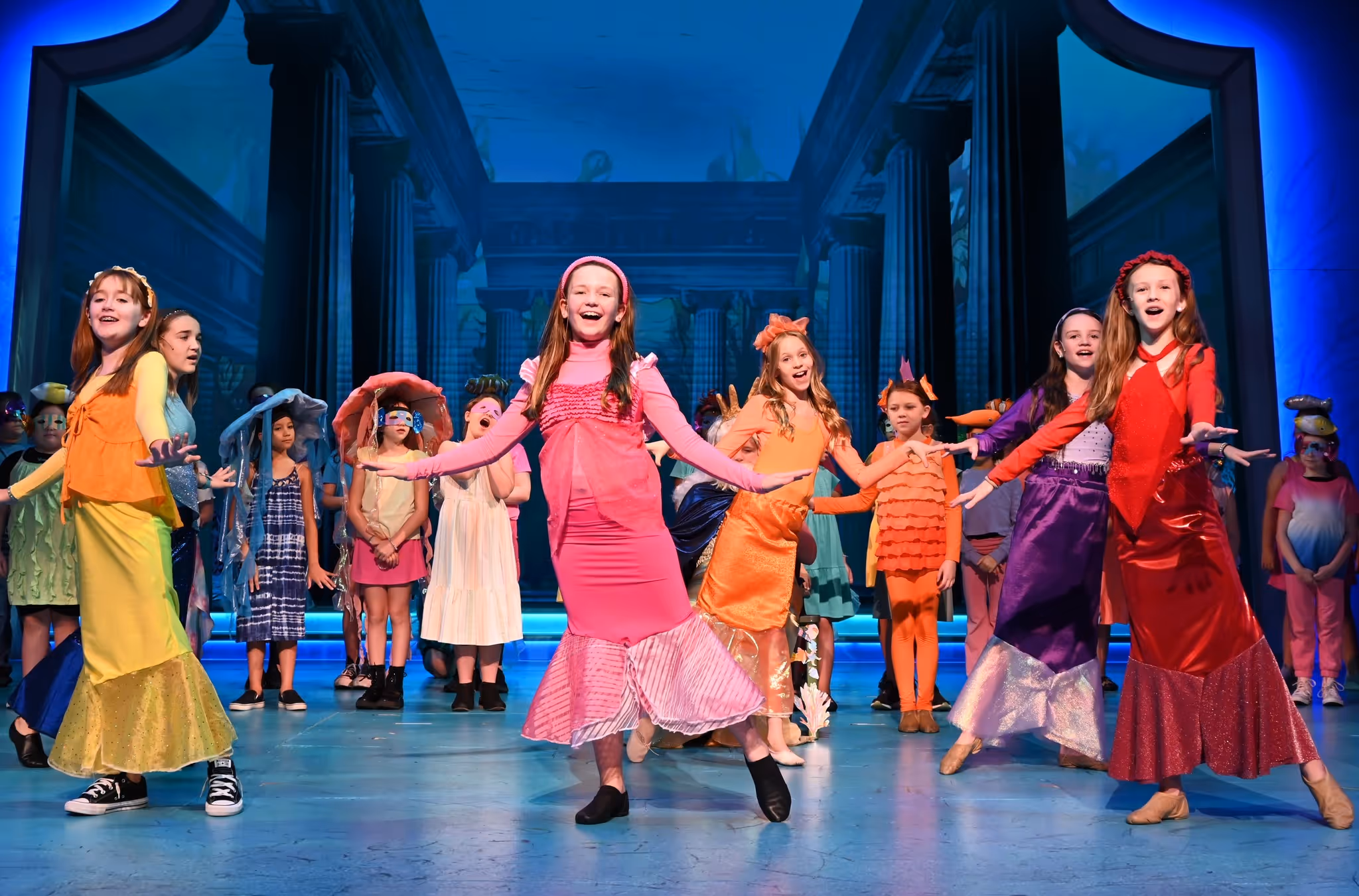 A group of young actresses dance wearing mermaid costumes.
