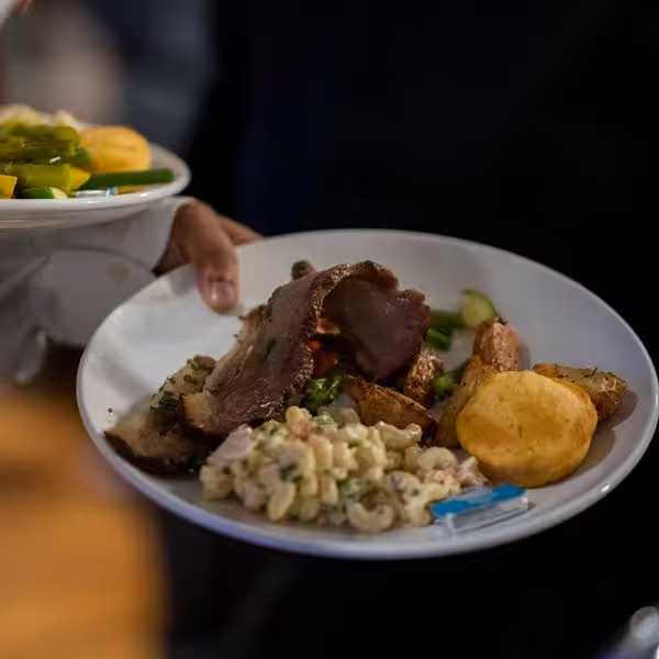 A plate of dinner food is carried to a guest's table.