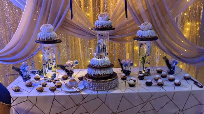 Intricate wedding cakes and cupcakes displayed on a white table.