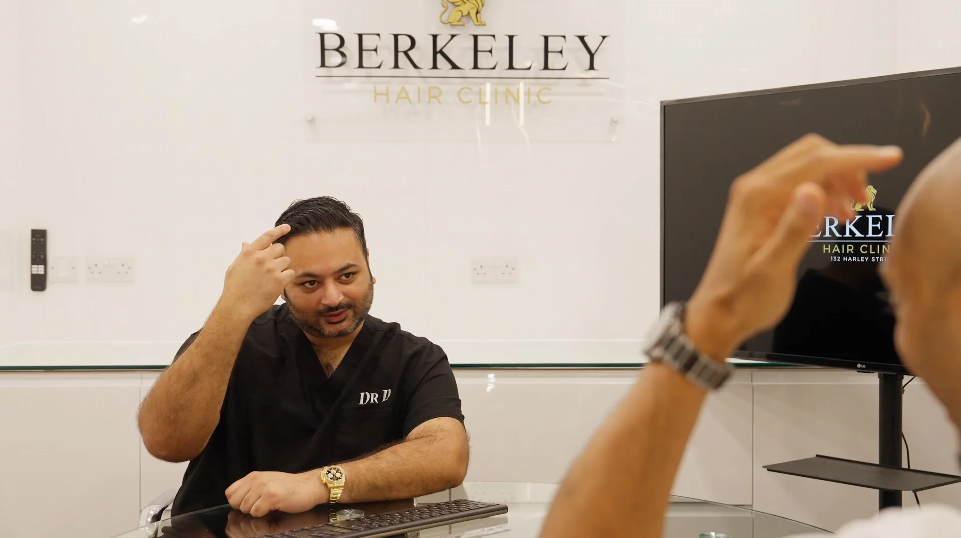 A doctor in black scrubs explaining hair treatment to a seated patient in Berkeley Hair Clinic.