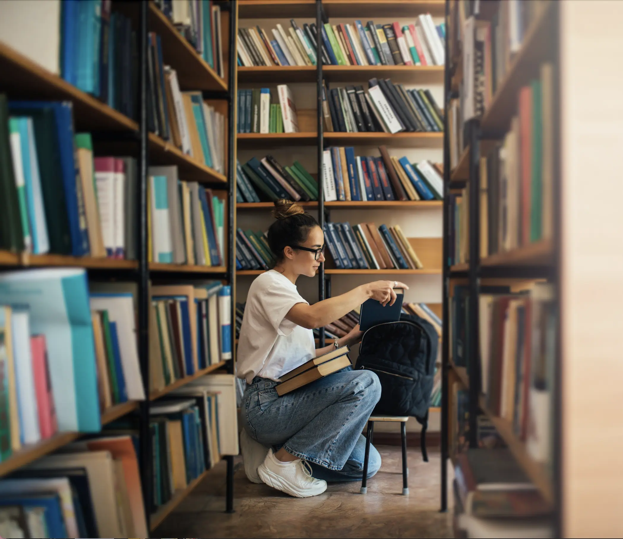 A girl in a library placing books into her bag.
