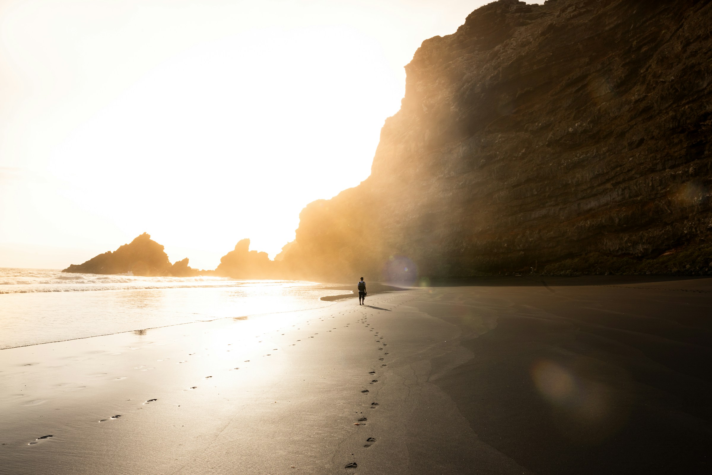 man walking down a beach towards the sun