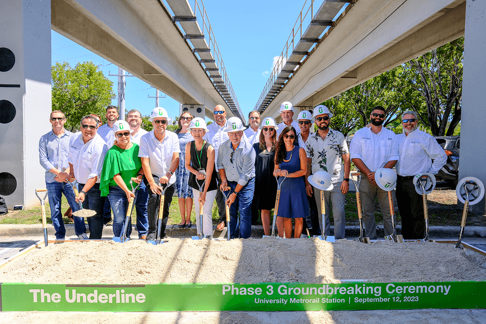 Group of people wearing hard hats and holding shovels at The Underline Phase 3 Groundbreaking Ceremony under elevated train tracks on a sunny day.