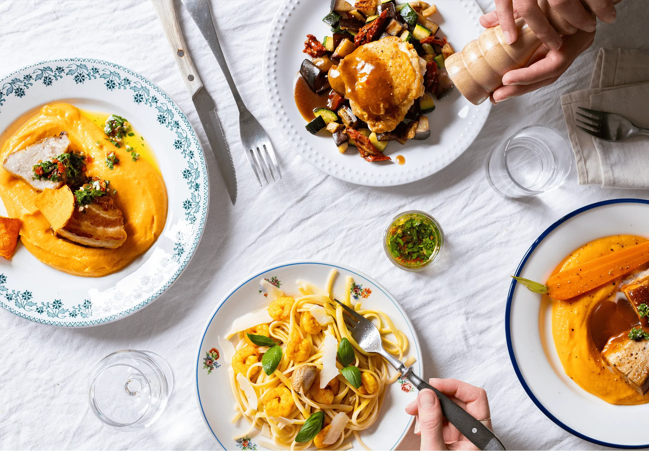 Table dressée avec différents plats cuisinés par Popchef : une purée de carottes avec de la viande, une ratatouille avec du poulet, des pates aux crevettes et champignons