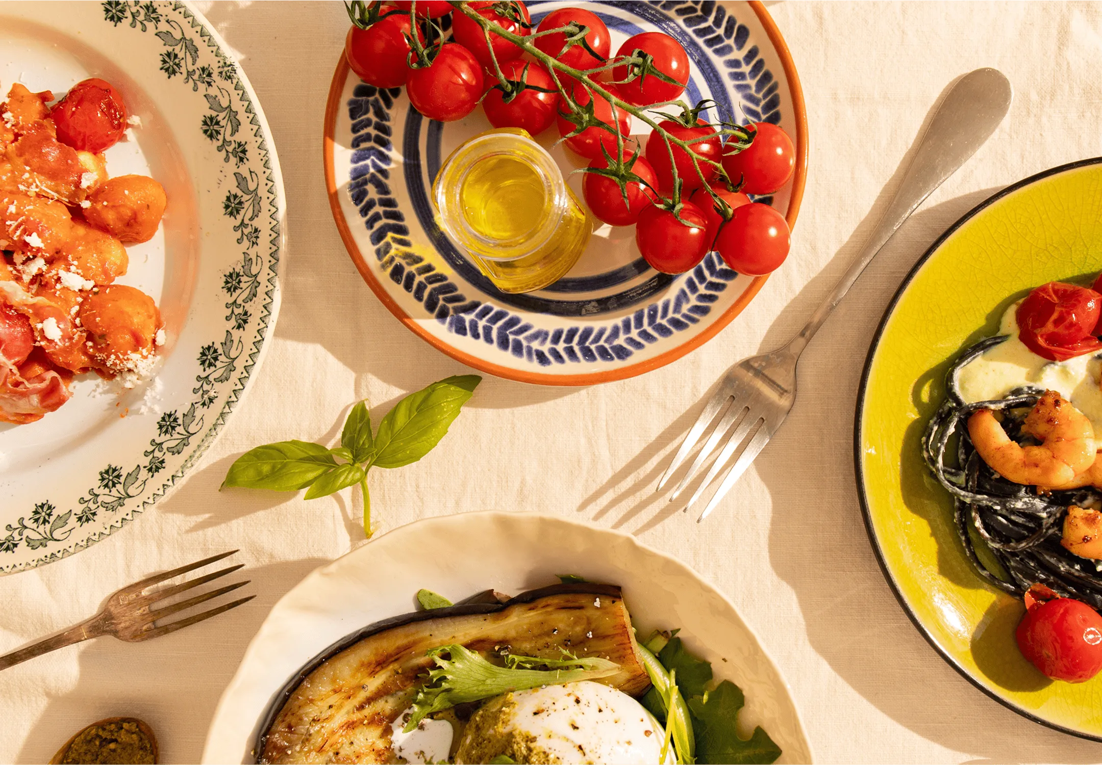 Table dressée avec différents plats cuisinés par Popchef : gnocchis à la tomate, pâtes aux crevettes, burrata avec légumes grillés et tomates cerises