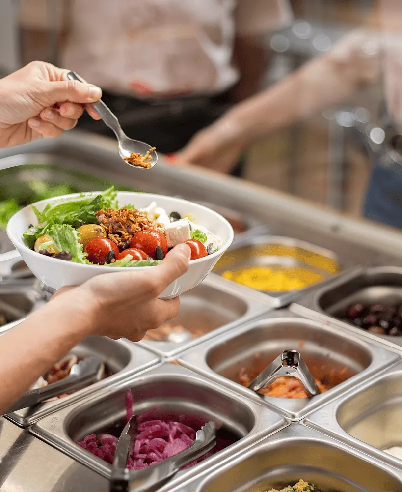 une personne ajoute des oignons frits dans une salade composée qu'elle prépare dans la cantine